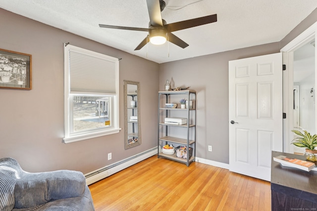 sitting room with light wood finished floors, a baseboard radiator, a ceiling fan, a textured ceiling, and baseboards