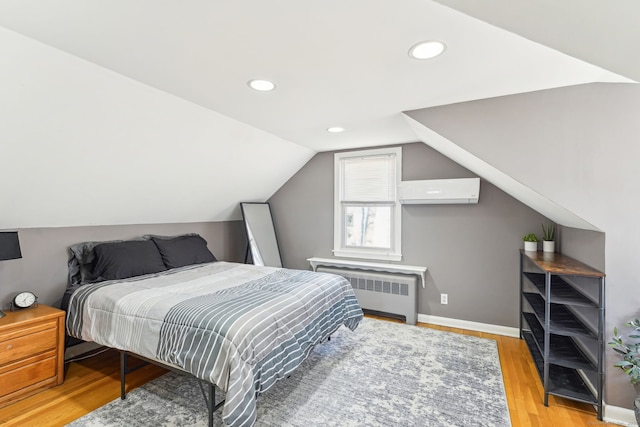 bedroom featuring a wall unit AC, lofted ceiling, radiator heating unit, light wood-type flooring, and baseboards