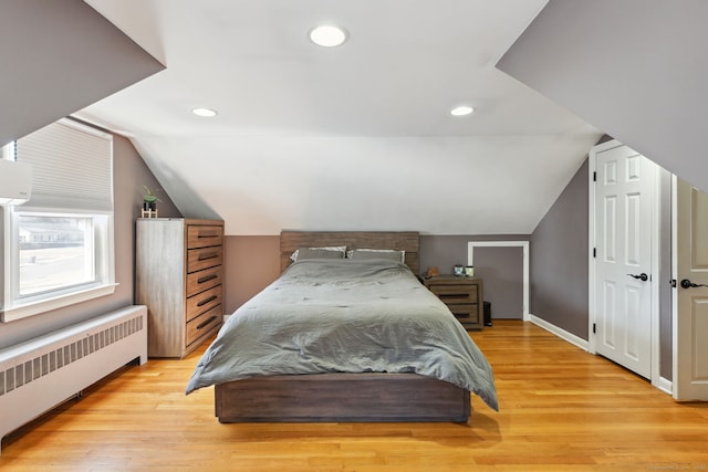 bedroom with light wood-style floors, lofted ceiling, baseboards, and radiator heating unit