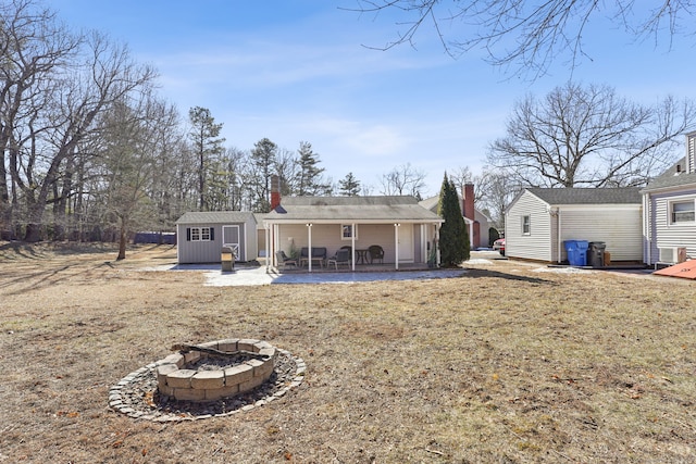 rear view of property with a storage shed, a fire pit, a patio, a chimney, and an outdoor structure