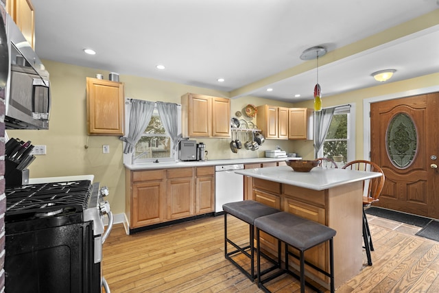 kitchen with light brown cabinetry, a breakfast bar area, hanging light fixtures, stainless steel appliances, and light wood-type flooring