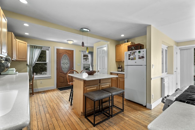 kitchen with a kitchen bar, a center island, light hardwood / wood-style flooring, white fridge, and pendant lighting