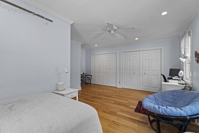 bedroom with crown molding, light hardwood / wood-style floors, ceiling fan, and two closets