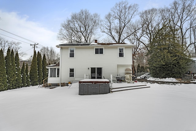 snow covered rear of property featuring a hot tub and a sunroom