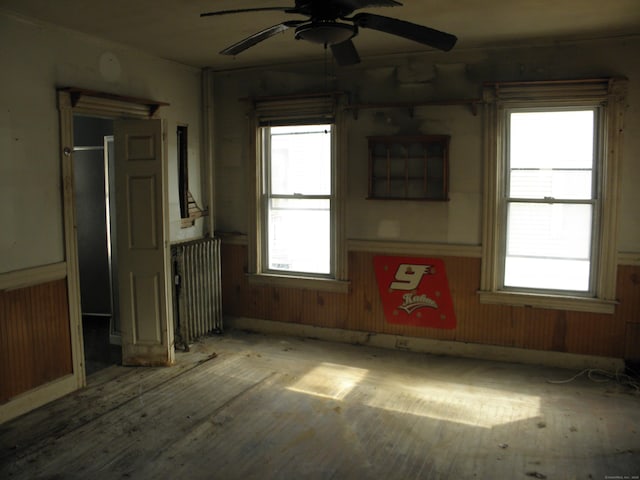 spare room with ceiling fan, a healthy amount of sunlight, radiator, and light wood-type flooring