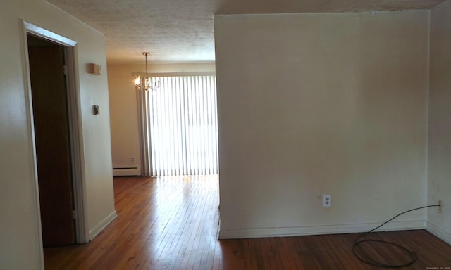 unfurnished room with a baseboard heating unit, a textured ceiling, wood finished floors, a chandelier, and baseboards