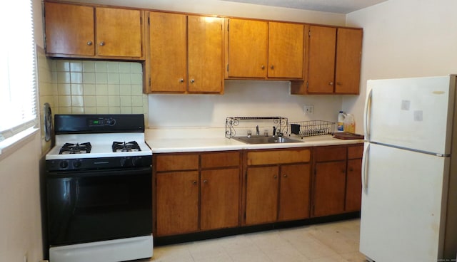 kitchen featuring a sink, light countertops, freestanding refrigerator, tasteful backsplash, and gas range oven