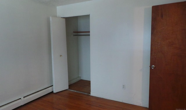 unfurnished bedroom with a baseboard radiator, a closet, baseboards, and wood finished floors