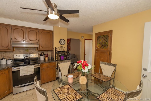 kitchen featuring stainless steel electric stove, light tile patterned floors, backsplash, and a textured ceiling