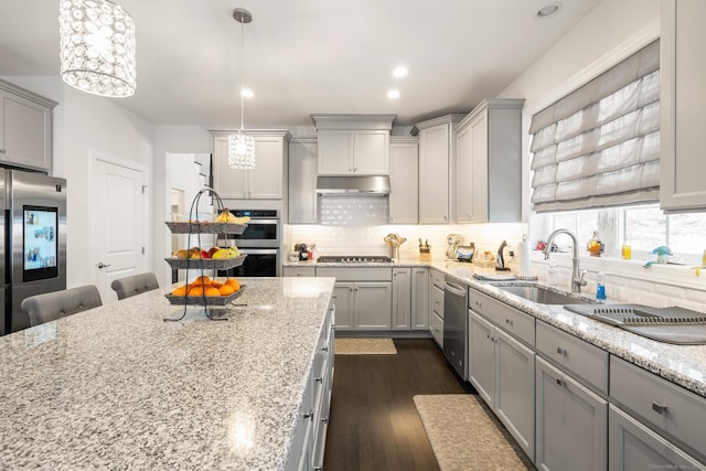 kitchen featuring pendant lighting, stainless steel appliances, light stone countertops, and sink