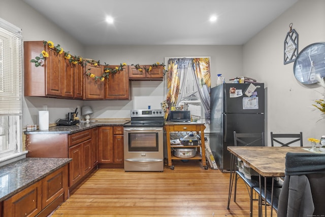 kitchen with dark stone countertops, black appliances, and light wood-type flooring