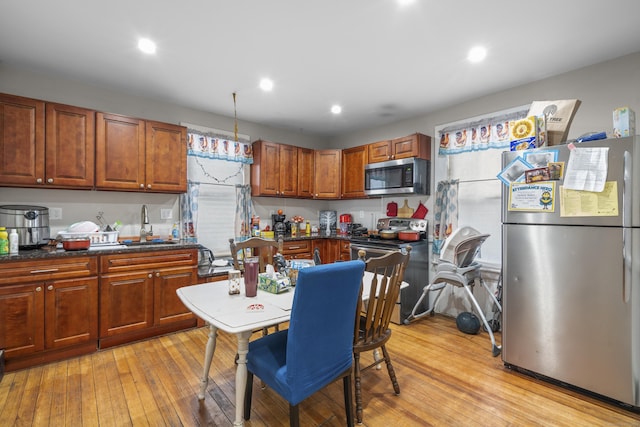 kitchen with pendant lighting, appliances with stainless steel finishes, sink, and light wood-type flooring