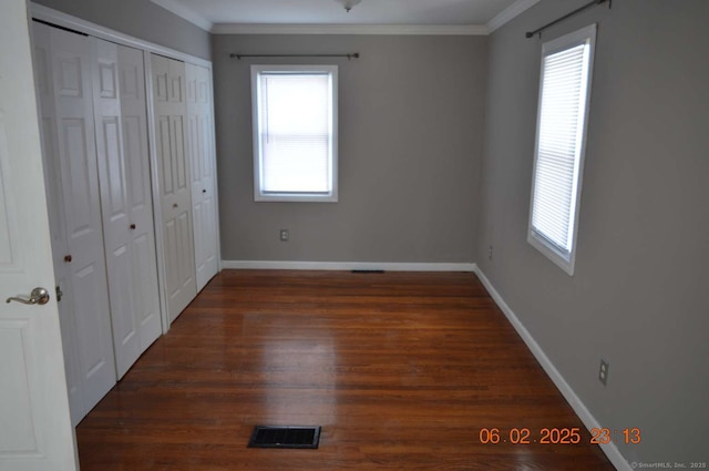 unfurnished bedroom featuring dark wood-type flooring, ornamental molding, and a closet