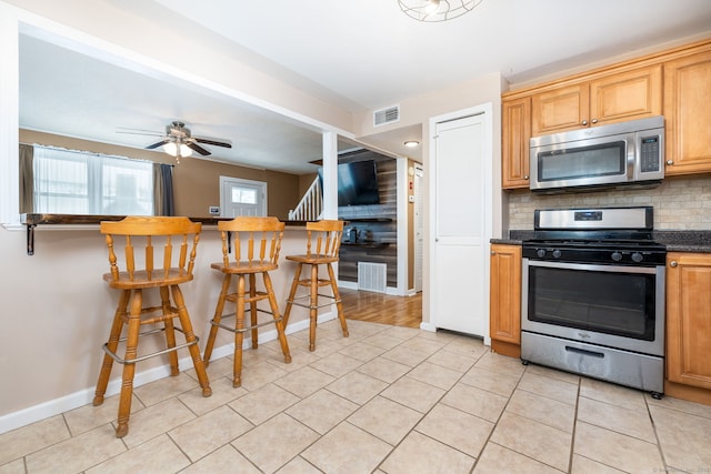 kitchen featuring appliances with stainless steel finishes, light tile patterned floors, a kitchen breakfast bar, and decorative backsplash