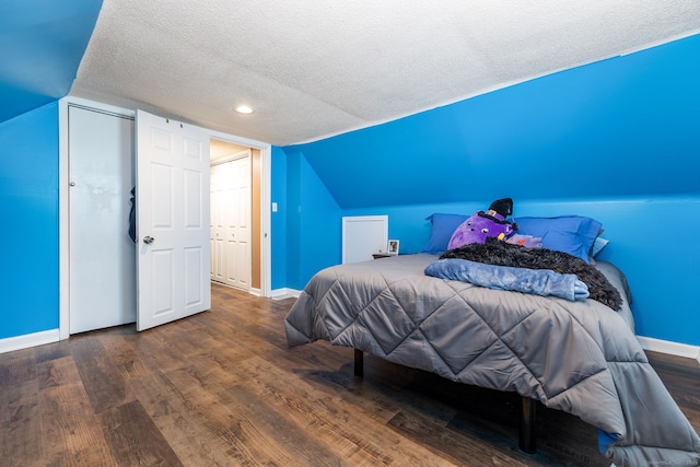 bedroom with vaulted ceiling, hardwood / wood-style floors, and a textured ceiling