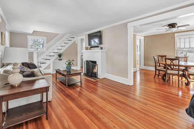 living room featuring ceiling fan, ornamental molding, light hardwood / wood-style floors, and a brick fireplace