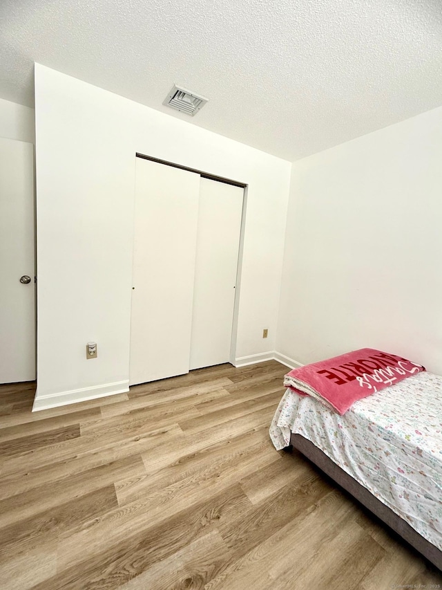 bedroom with light hardwood / wood-style floors, a closet, and a textured ceiling