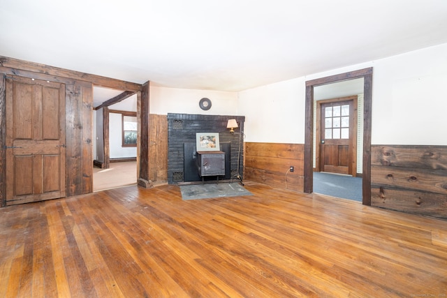 unfurnished living room featuring hardwood / wood-style flooring, wooden walls, and a wood stove