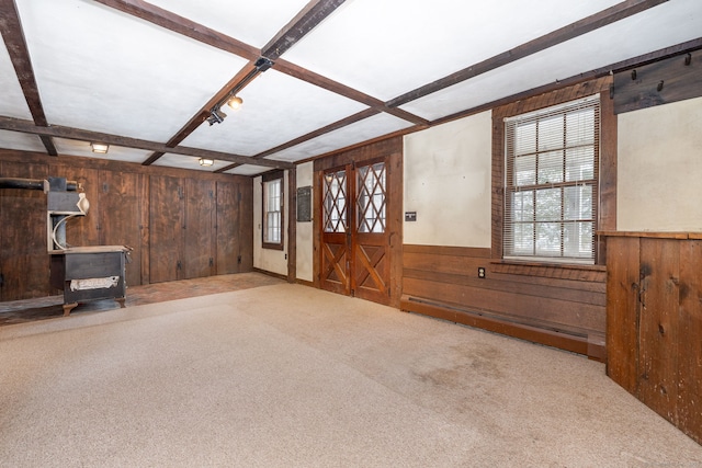 unfurnished living room with coffered ceiling, light carpet, a baseboard radiator, wooden walls, and beam ceiling