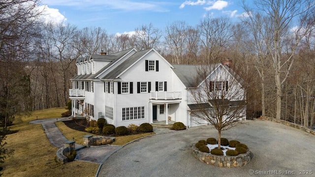 view of front of property featuring a chimney, driveway, and a balcony