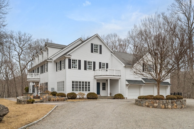 view of front of home featuring roof with shingles, an attached garage, a balcony, and gravel driveway