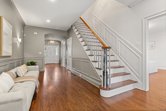 foyer featuring crown molding, a decorative wall, stairway, and wood finished floors