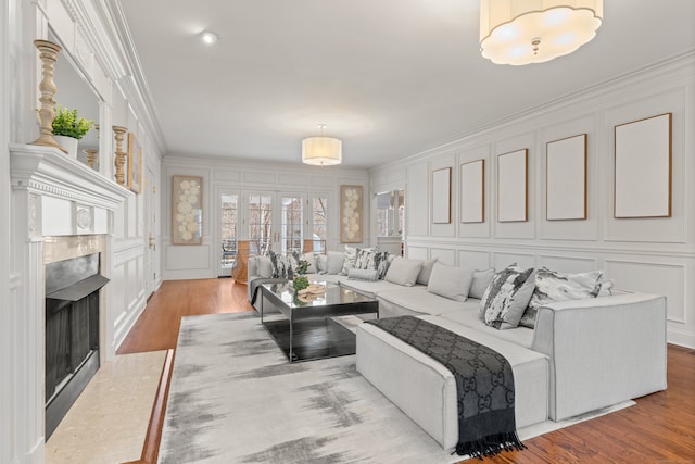 living area with ornamental molding, a decorative wall, wood finished floors, and a tile fireplace