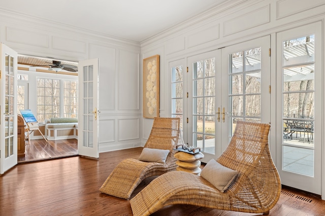 sitting room featuring a decorative wall, wood finished floors, visible vents, french doors, and crown molding