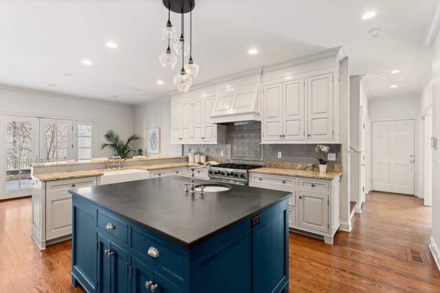 kitchen featuring blue cabinets, a peninsula, premium range hood, a sink, and high end stainless steel range oven