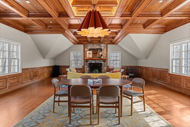 dining space featuring light wood finished floors, wood ceiling, a wainscoted wall, and a stone fireplace