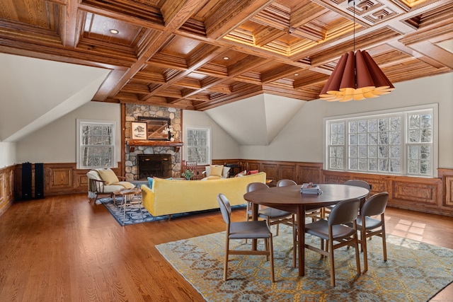 dining room with light wood finished floors, wood ceiling, wainscoting, and a stone fireplace