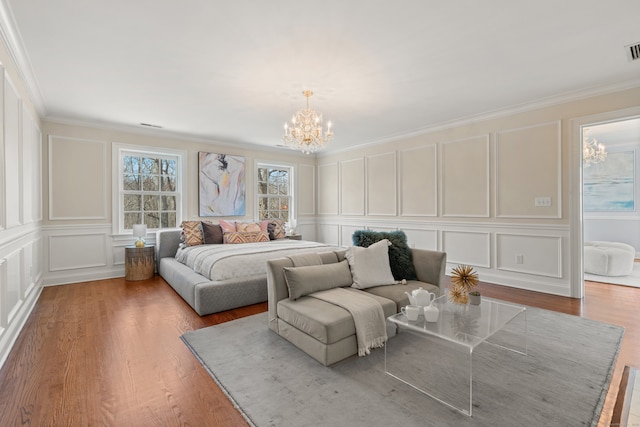 bedroom with a notable chandelier, a decorative wall, wood finished floors, visible vents, and crown molding