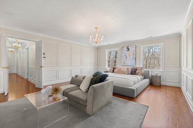 bedroom featuring a chandelier, a decorative wall, wood finished floors, and ornamental molding