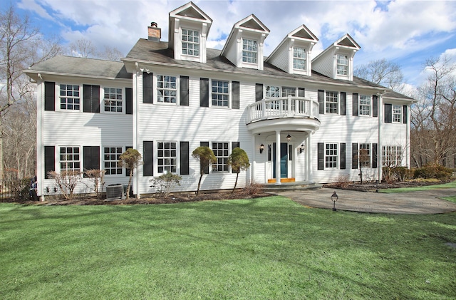 colonial house featuring a chimney, central AC, a balcony, and a front lawn