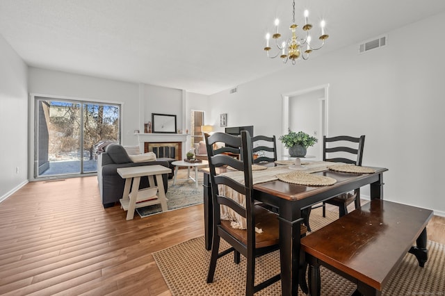 dining area featuring a brick fireplace, an inviting chandelier, and wood-type flooring