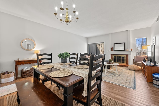 dining area with wood finished floors, a glass covered fireplace, and an inviting chandelier