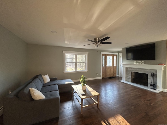 living room with dark wood-style floors, a fireplace with raised hearth, baseboards, and ceiling fan