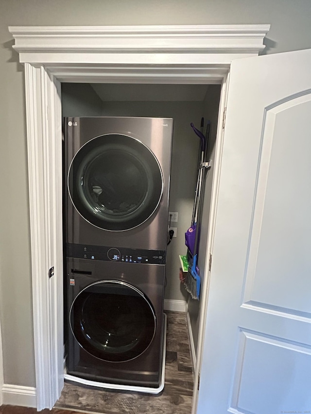 laundry room with laundry area, stacked washer / drying machine, baseboards, and wood finished floors