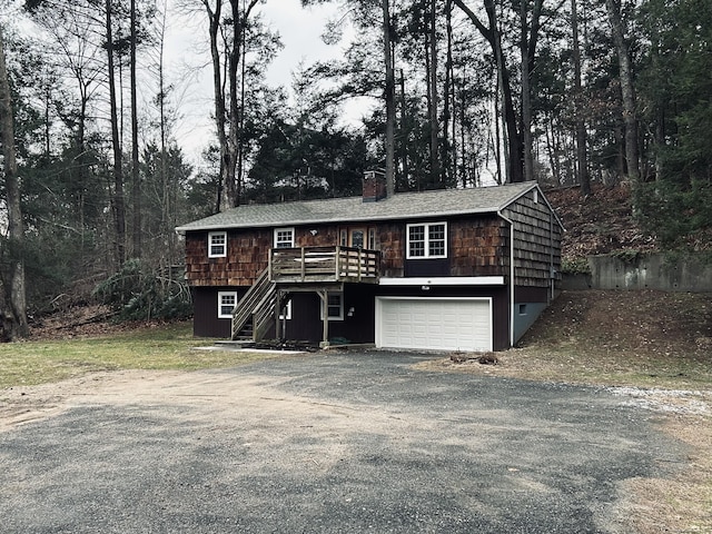 view of front of home with stairway, driveway, a wooden deck, an attached garage, and a chimney