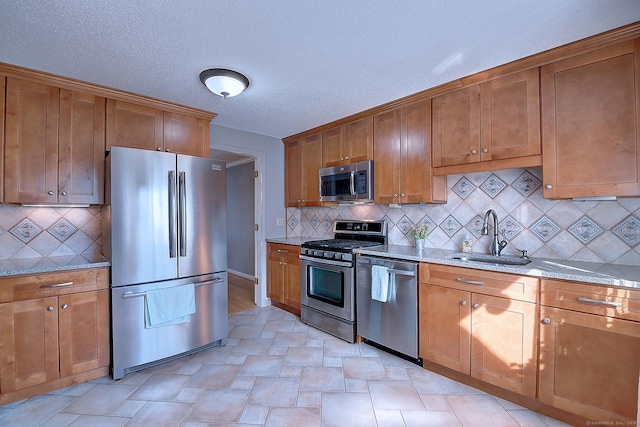 kitchen featuring brown cabinetry, appliances with stainless steel finishes, light stone countertops, and a sink