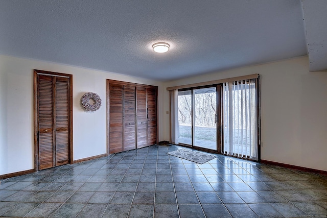 unfurnished bedroom featuring baseboards, tile patterned flooring, multiple closets, a textured ceiling, and access to outside