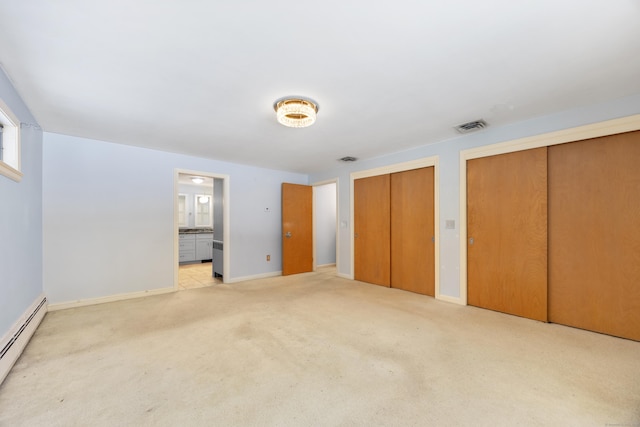 unfurnished bedroom featuring two closets, light colored carpet, baseboard heating, and ensuite bath