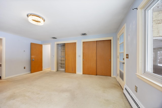 unfurnished bedroom with multiple closets, light carpet, and a baseboard heating unit