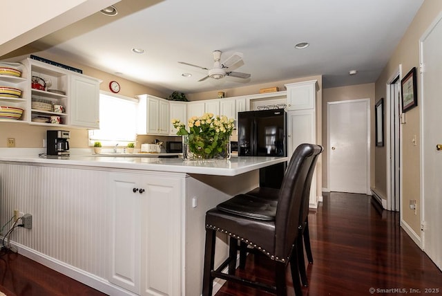 kitchen with black fridge, a kitchen breakfast bar, dark hardwood / wood-style flooring, kitchen peninsula, and white cabinets