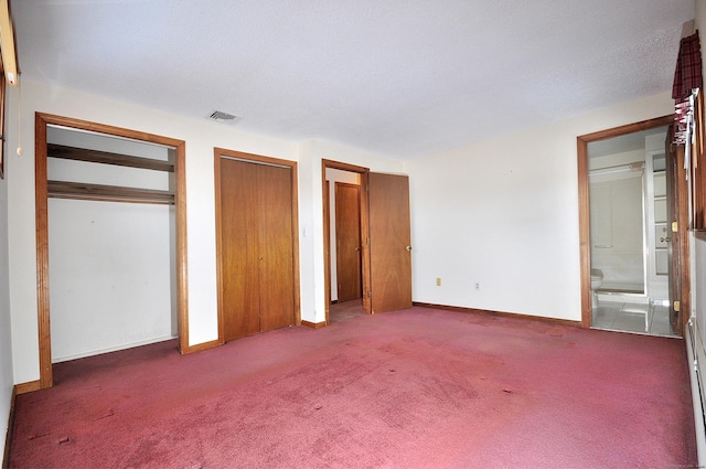 unfurnished bedroom with connected bathroom, two closets, and dark colored carpet