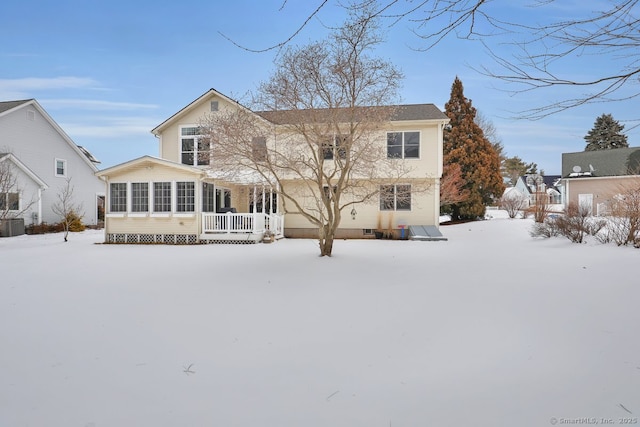 snow covered rear of property with a sunroom