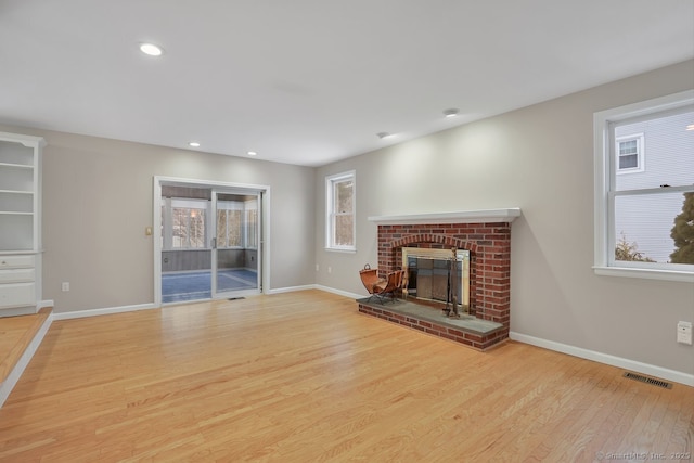 unfurnished living room with a fireplace, wood finished floors, visible vents, and baseboards