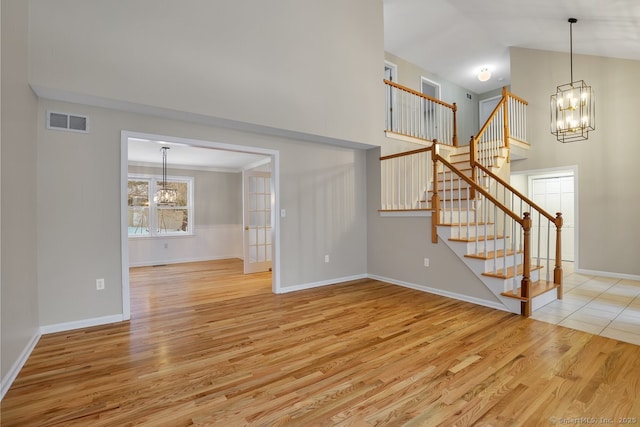 unfurnished living room featuring high vaulted ceiling, a chandelier, and light hardwood / wood-style flooring