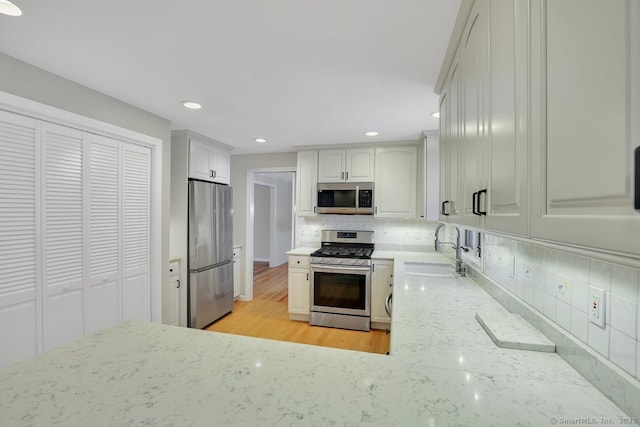 kitchen featuring sink, light stone counters, light wood-type flooring, stainless steel appliances, and decorative backsplash