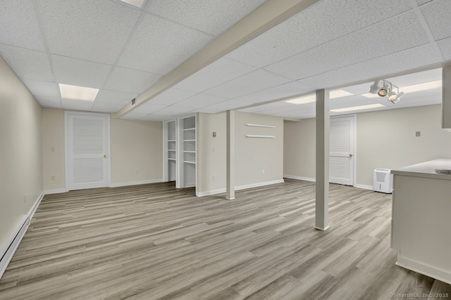 finished below grade area featuring a baseboard radiator, baseboards, light wood finished floors, and a paneled ceiling